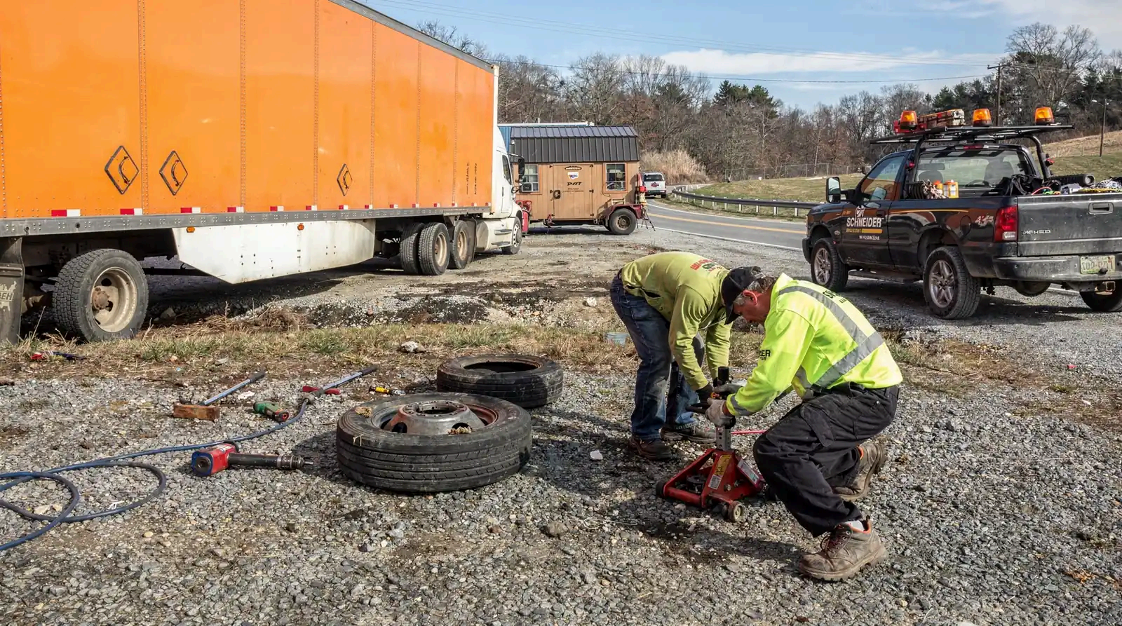 Two mechanics working on a semi truck brake and wheel system on the side of a road near Charleston, WV