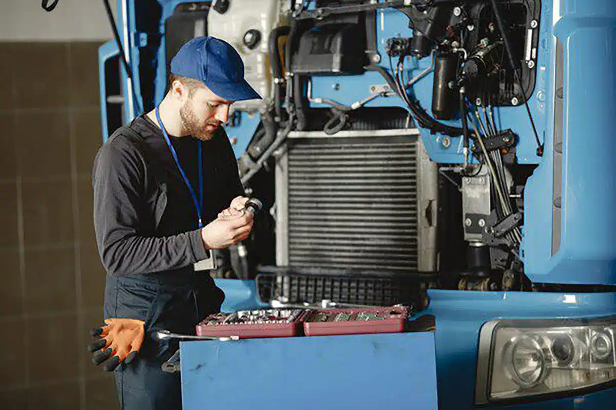 Heavy-duty truck technician diagnosing electrical components at the front of a semi truck