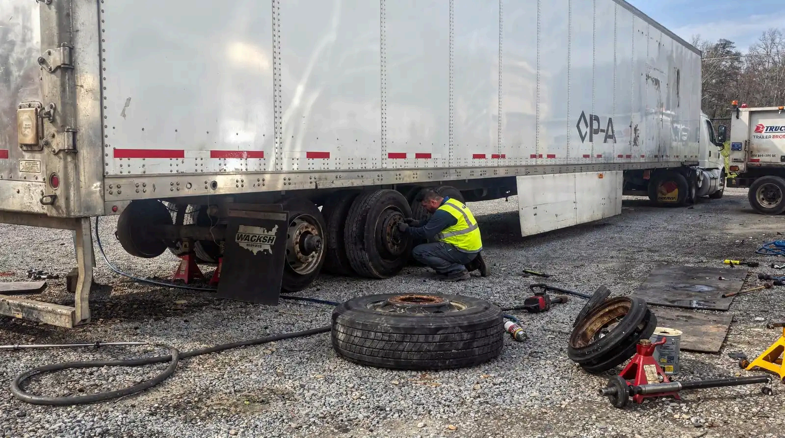 A CPA technician in a high-visibility vest repairing the brakes of a semi trailer on a gravel lot